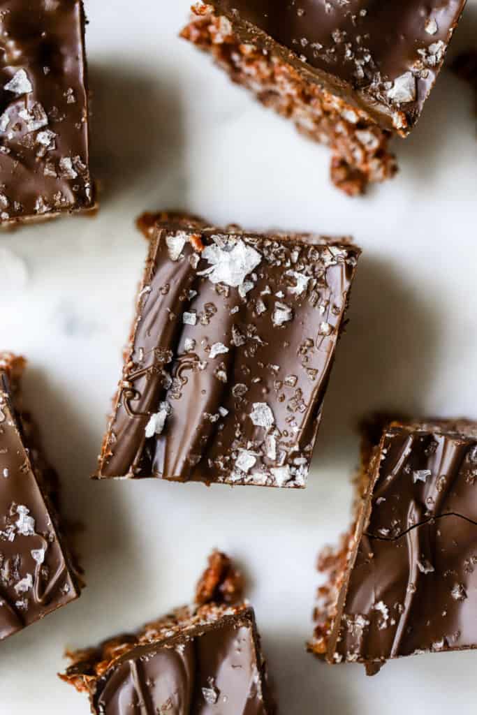 Five healthy scotcheroos topped with flaky sea salt and cut into squares on blue and white background