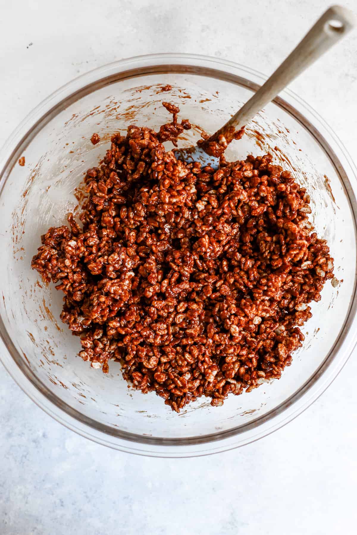 Date syrup and peanut butter mixture fully combined with brown rice crisps in a bowl.