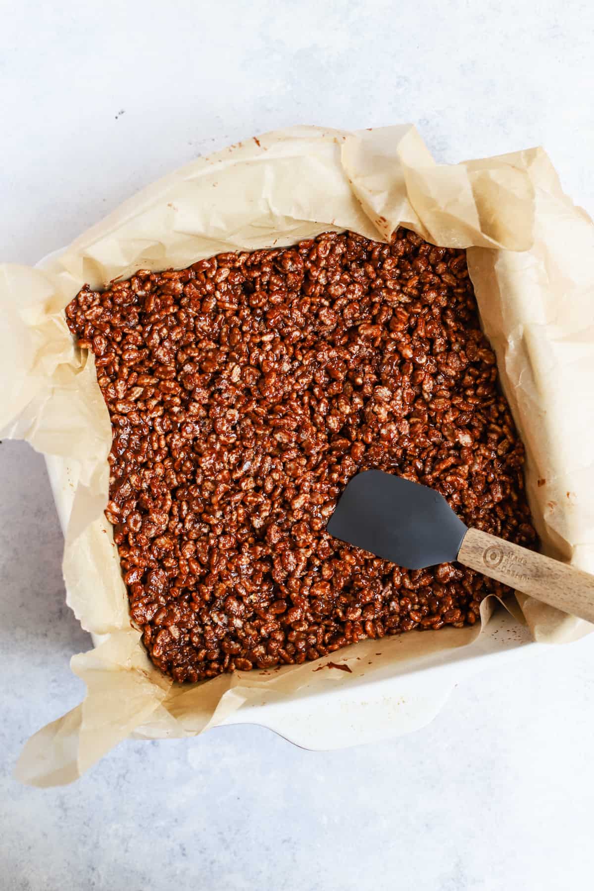 Brown rice crisp mixture being pressed into an 8x8 pan.