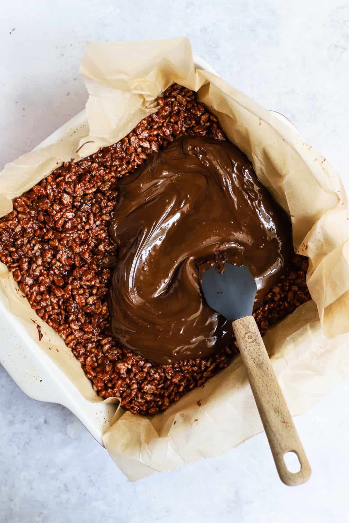 Brown rice crisp mixture pressed into pan with melted chocolate being spread over top.