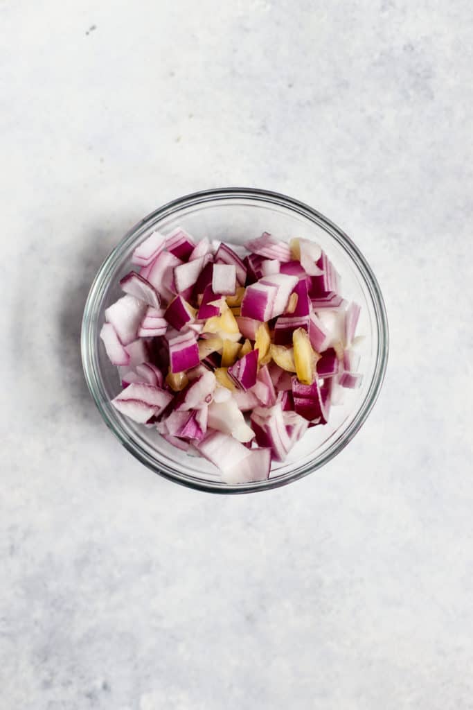 Diced red onions and sliced garlic in a small clear glass bowl