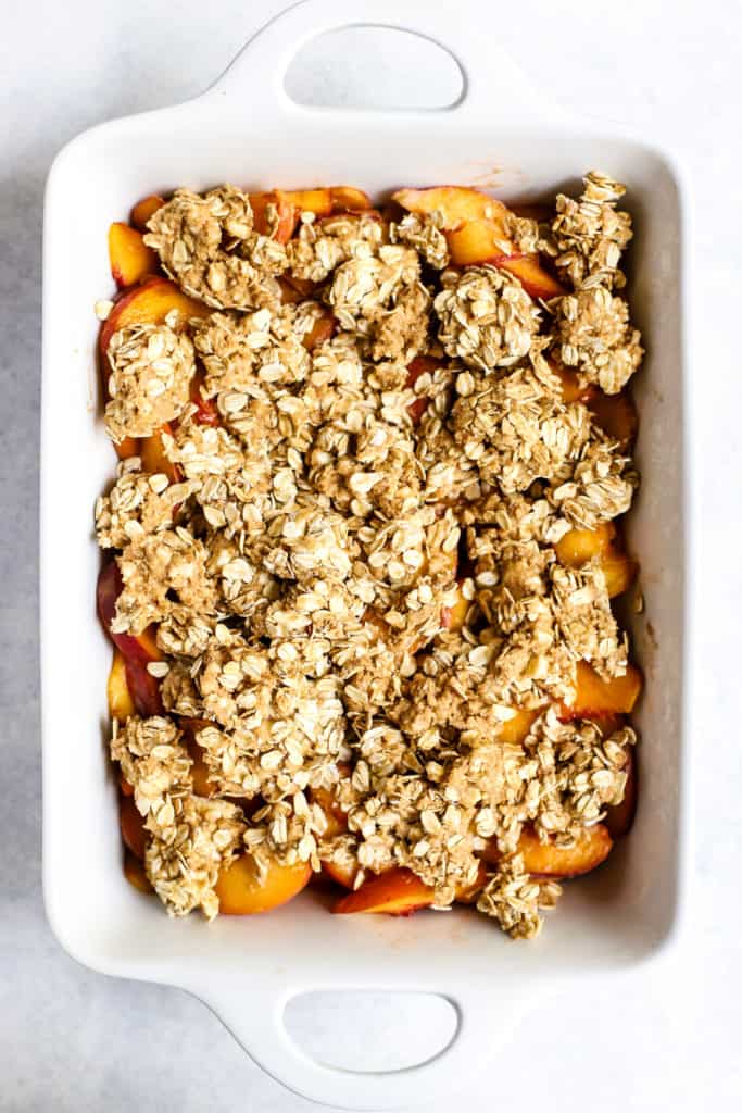 Healthy peach crisp before baking in white ceramic baking dish