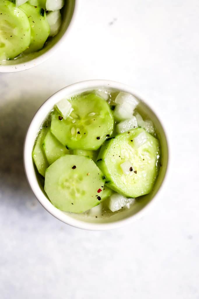 Vinegar cucumber salad in small white bowl with freshly cracked pepper on top.