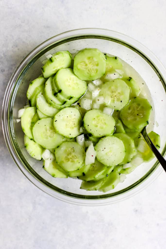 Vinegar cucumber salad in clear glass bowl with fresh cracked pepper on top and spoon
