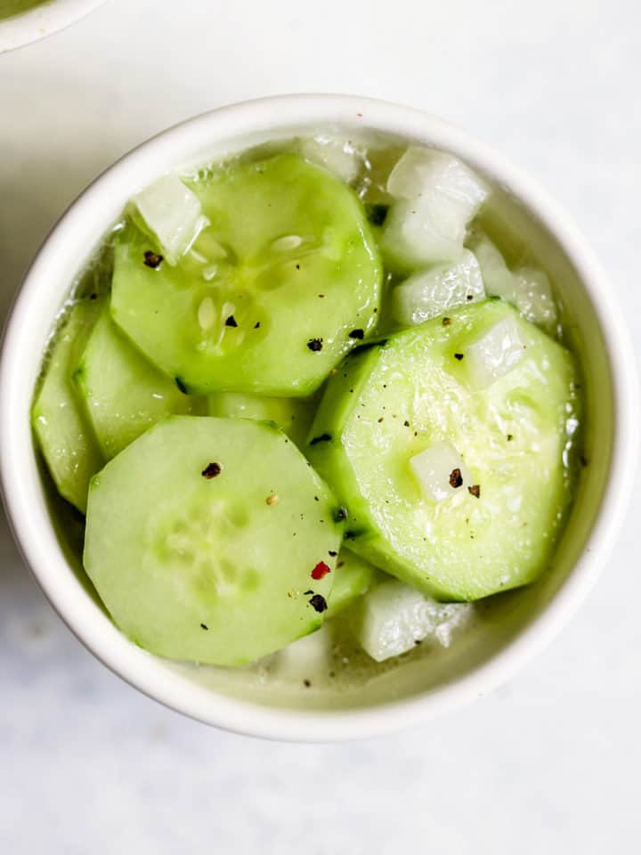 Vinegar cucumber salad in small white bowl with freshly cracked pepper on top