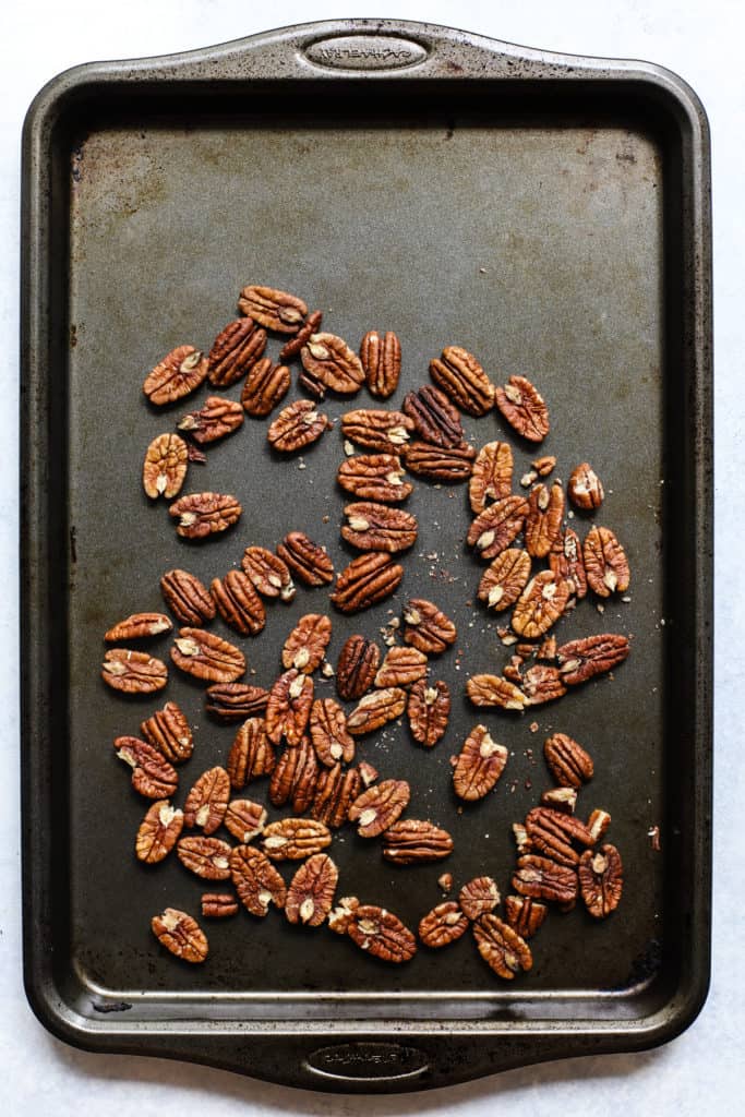 Toasted pecans on dark gray sheet pan.