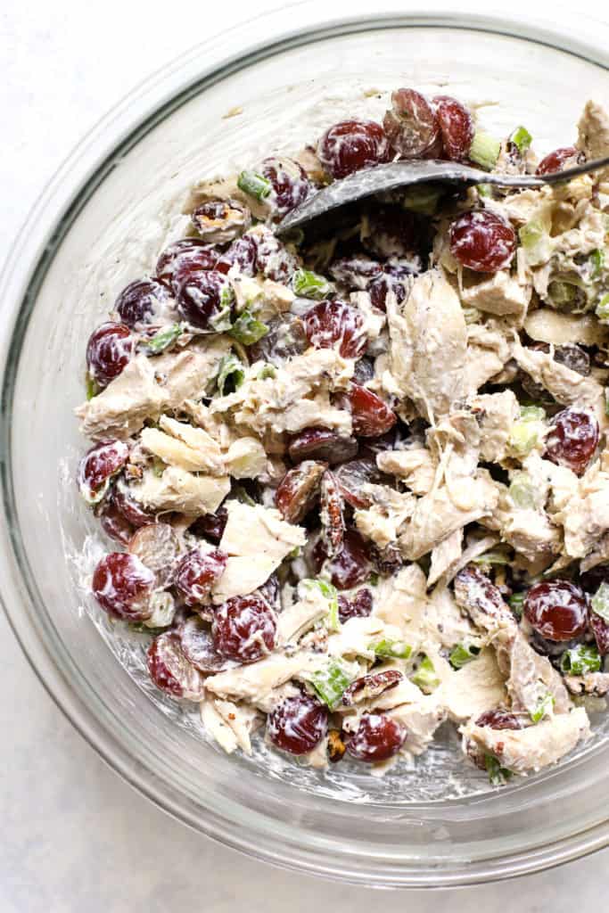 Healthy chicken salad with grapes and pecans mixed together in clear glass bowl.