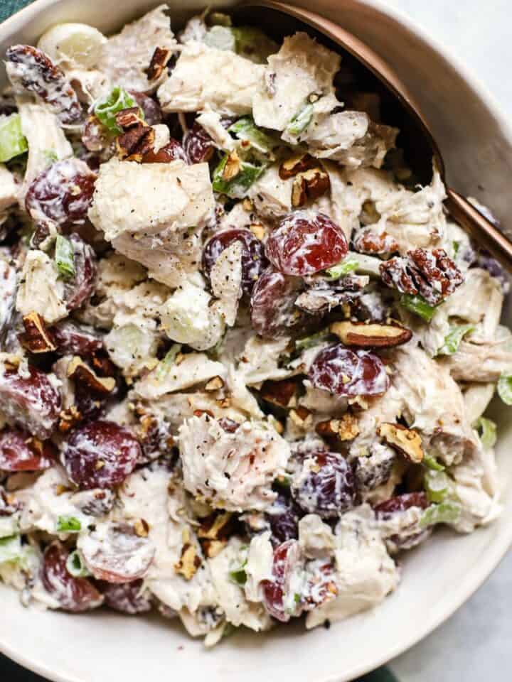 Chicken salad with grapes in white bowl with serving spoon.