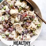 Chicken salad with grapes and pecans in white ceramic bowl with copper serving spoon on teal linen, on white and light blue surface