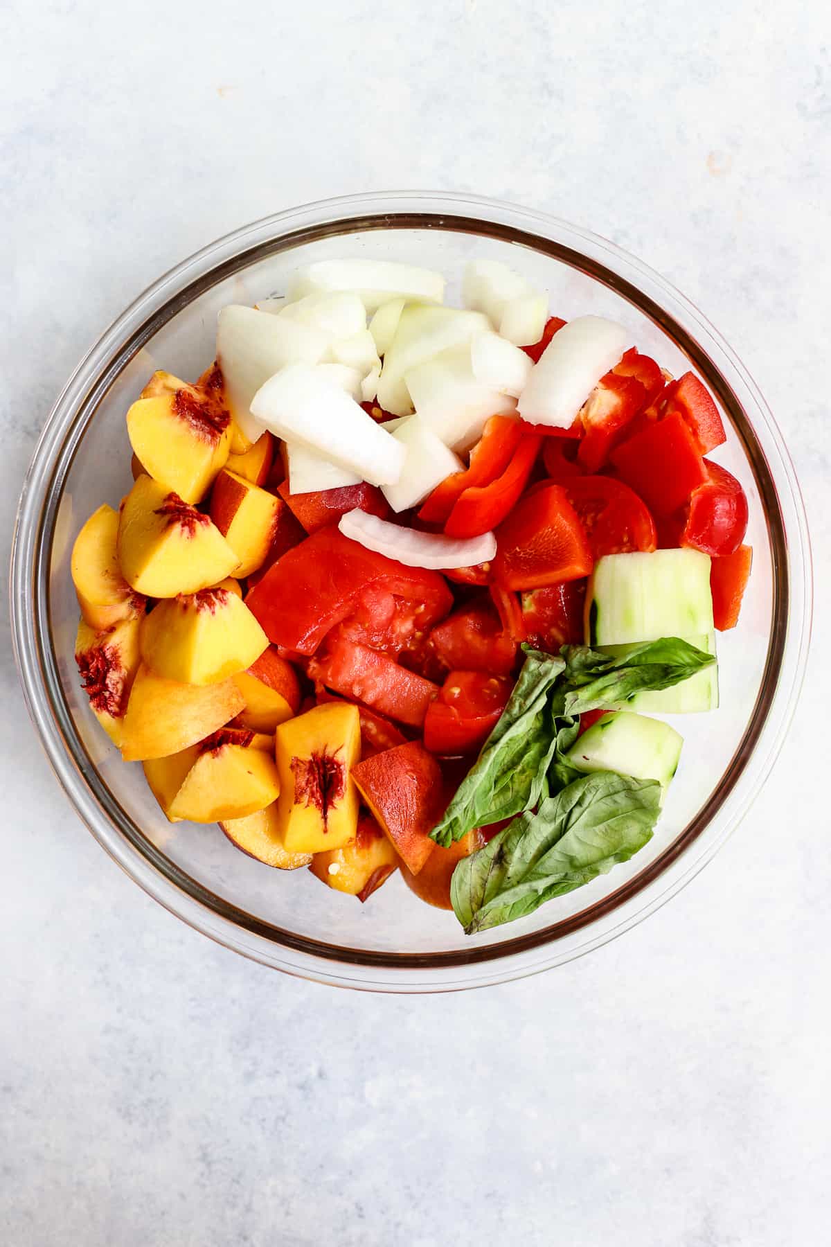 Peach basil gazpacho ingredients chopped, in glass bowl