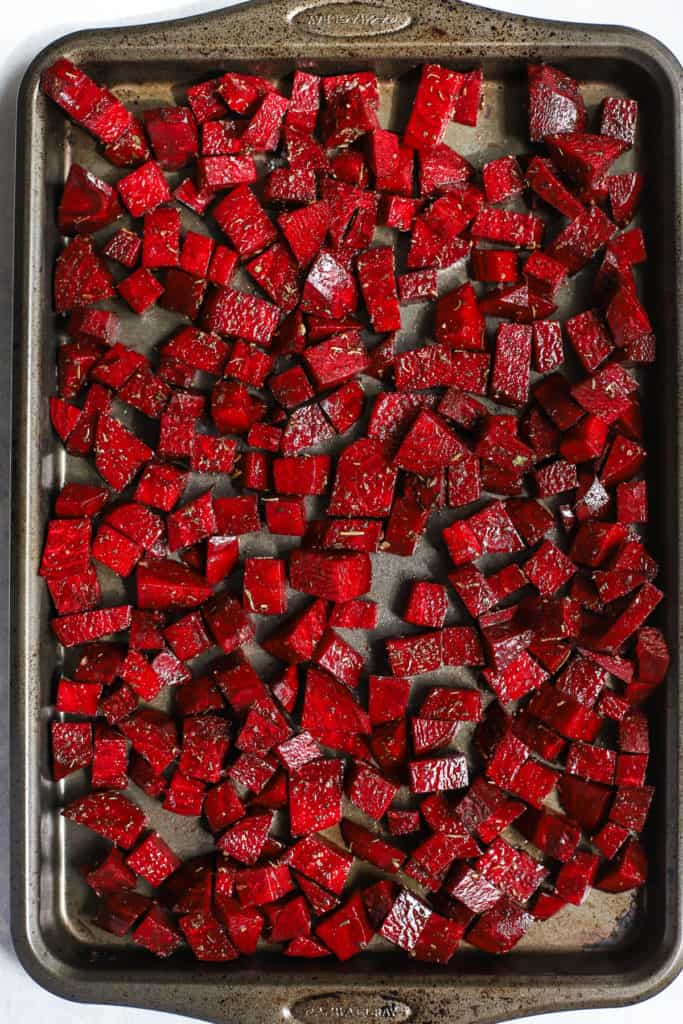 Cubed beets in olive oil and herbs de Provence on sheet pan, ready to be roasted.