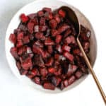 Simple herb roasted beets in white ceramic bowl with copper serving spoon on light blue background