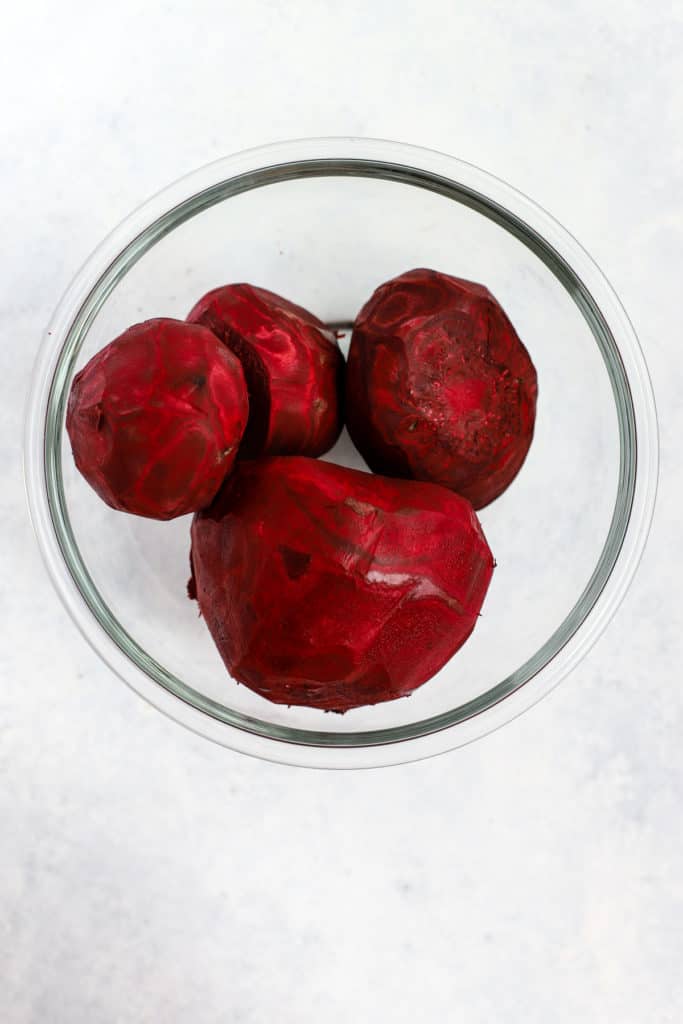 Peeled beets in clear glass bowl on light blue and white surface