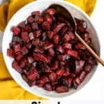 Simple herb roasted beets in white ceramic bowl with copper serving spoon on light blue background with golden yellow linen