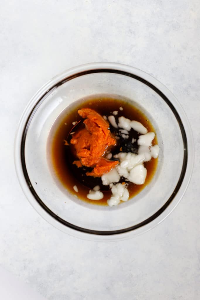 Maple syrup, coconut oil, pumpkin, and vanilla extract in clear glass bowl before being heated and mixed