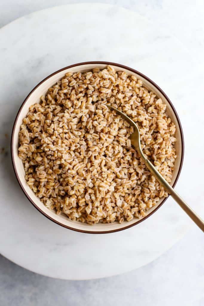 Cooked farro in tan dish with gold spoon