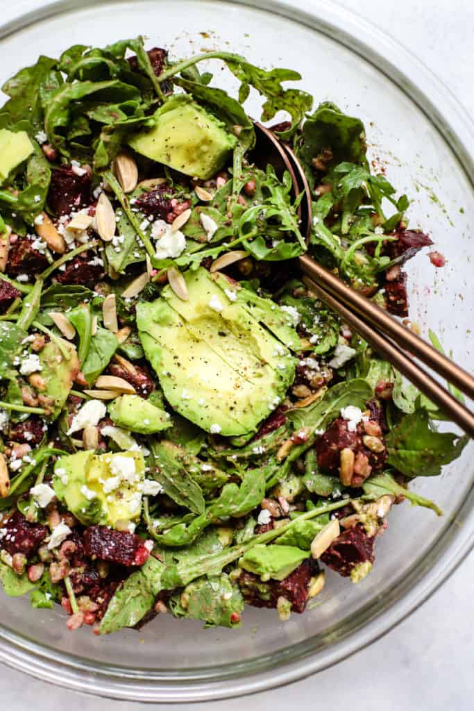 Roasted beet and avocado salad with copper serving spoons in large clear glass bowl