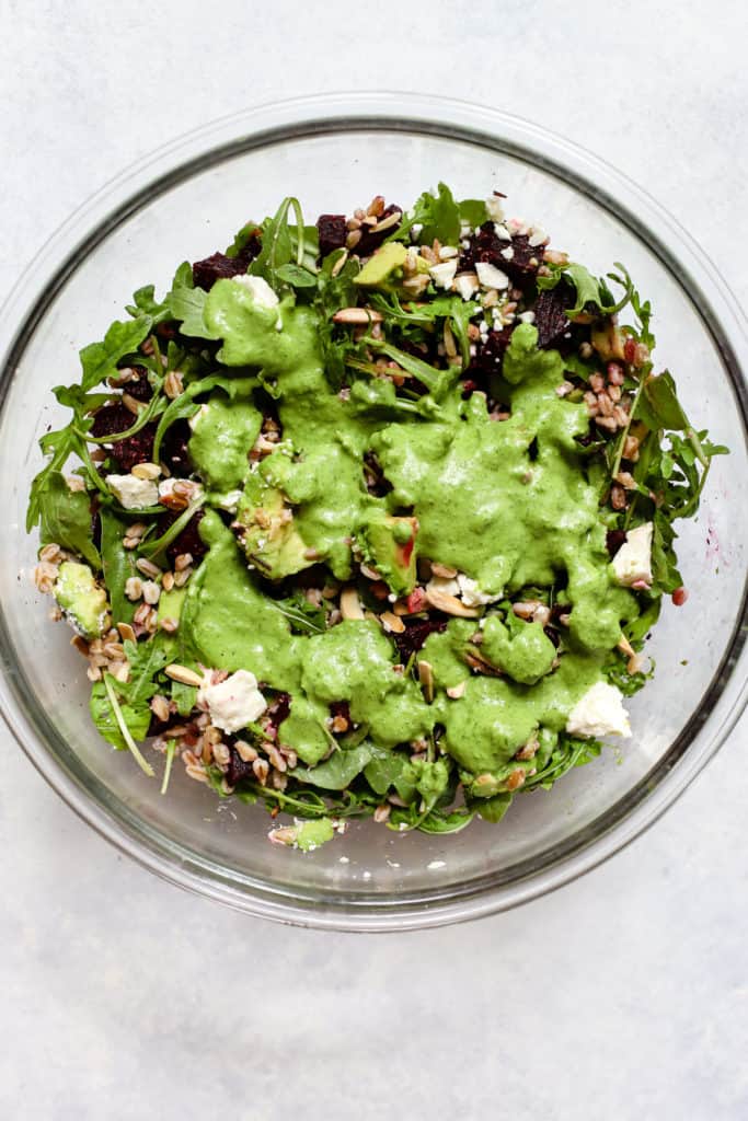 Basil lime vinaigrette poured over roasted beet and avocado salad, in large clear glass bowl