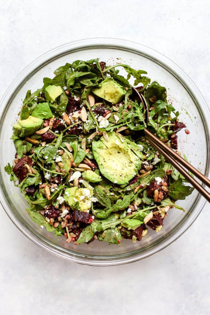 Roasted beet and avocado salad with copper serving spoons in large clear glass bowl