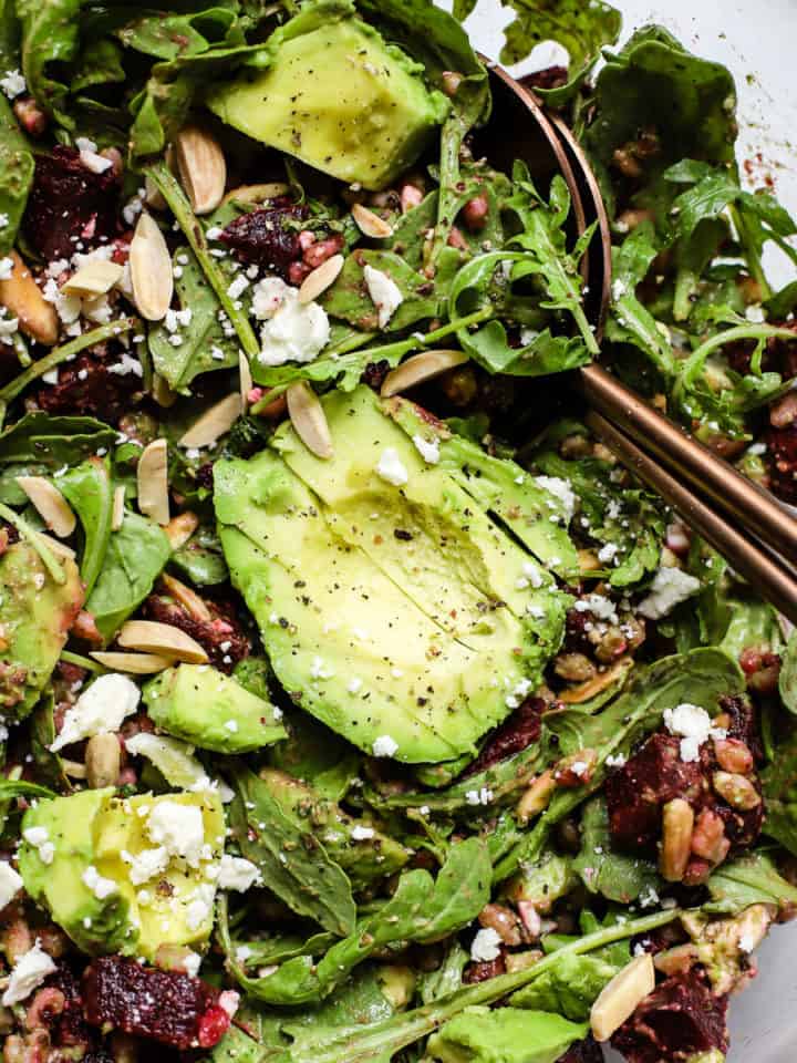 Roasted beet and avocado salad with copper serving spoons in large clear glass bowl