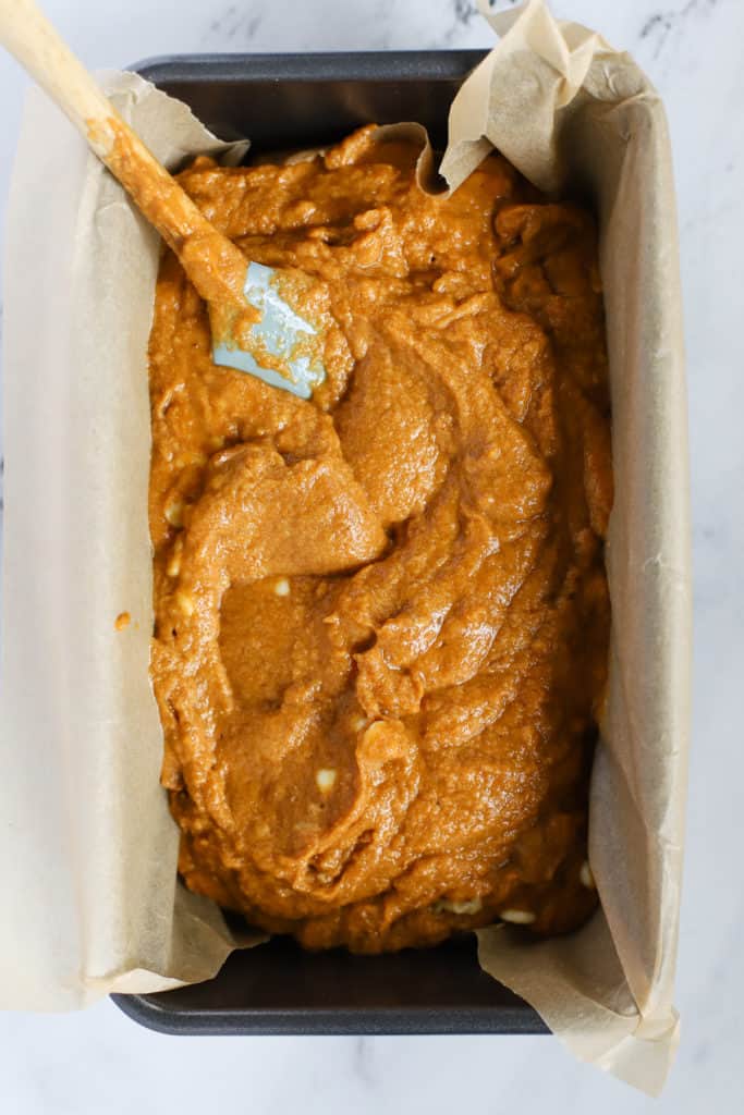 Healthy spelt pumpkin bread batter spread into bread pan lined with parchment paper, and mini spatula spreading batter