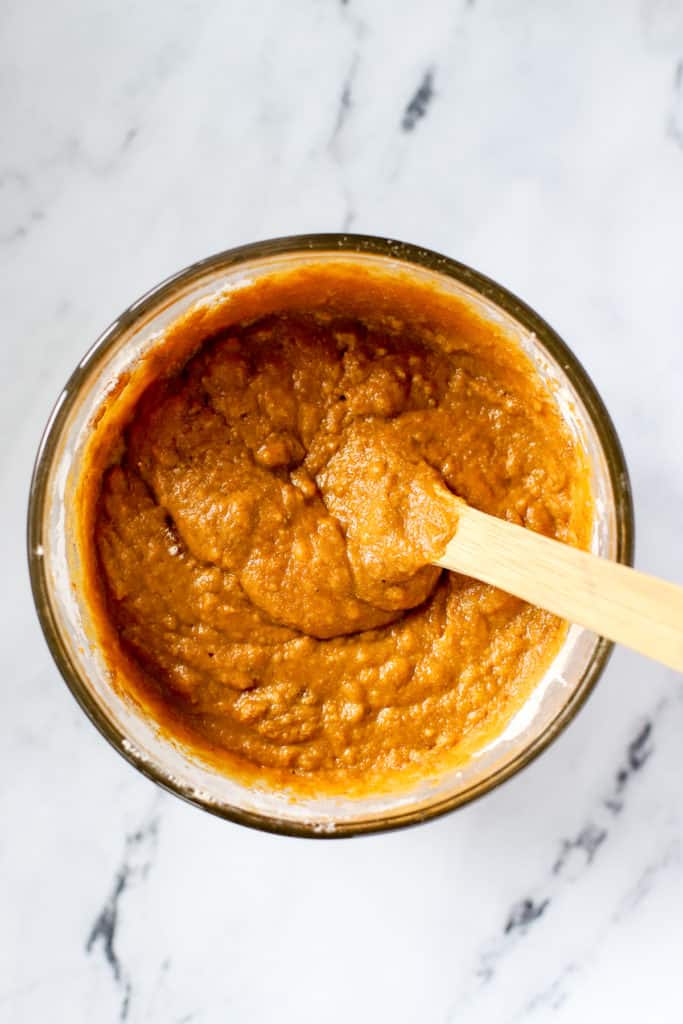 Healthy spelt pumpkin bread batter fully mixed in clear glass bowl with wooden spoon