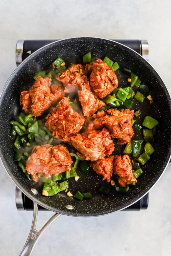 Ground chorizo cooking with poblano peppers and garlic in black sauté pan