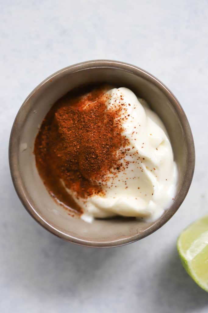 Chipotle mayo ingredients in small gray pinch bowl (mayo, chipotle seasoning, lime), with lime wedge on the side