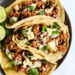 Three chorizo tacos and three lime wedges on gray plate, on light blue and white surface