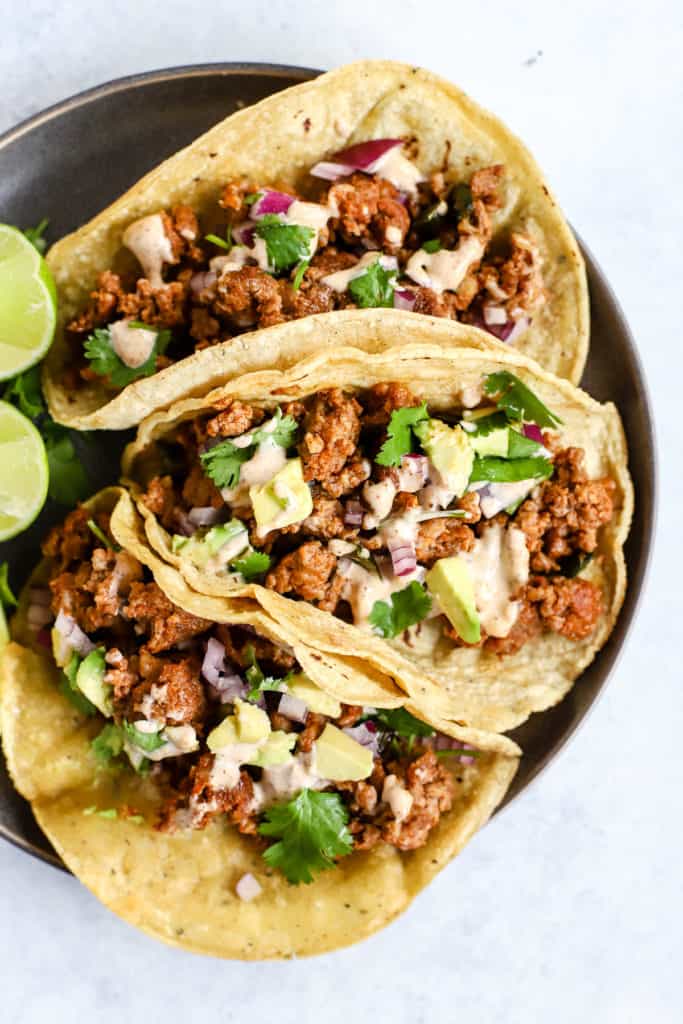 Three chorizo tacos and three lime wedges on gray plate, on light blue and white surface