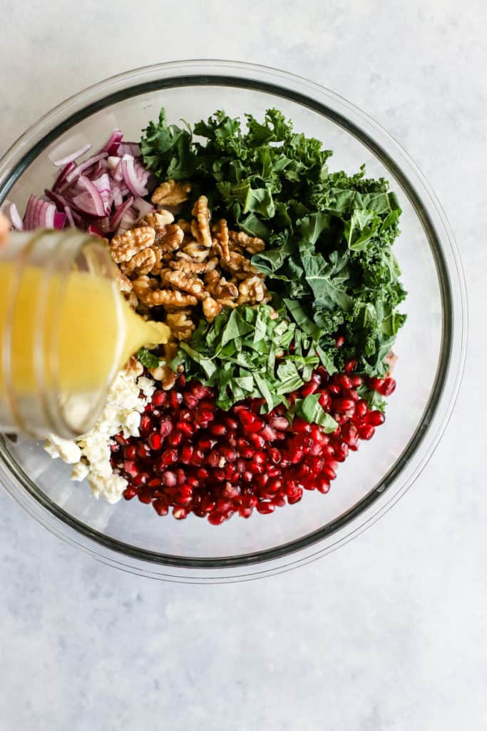 Wild rice and pomegranate salad ingredients in glass bowl with simple orange vinaigrette being poured over the top