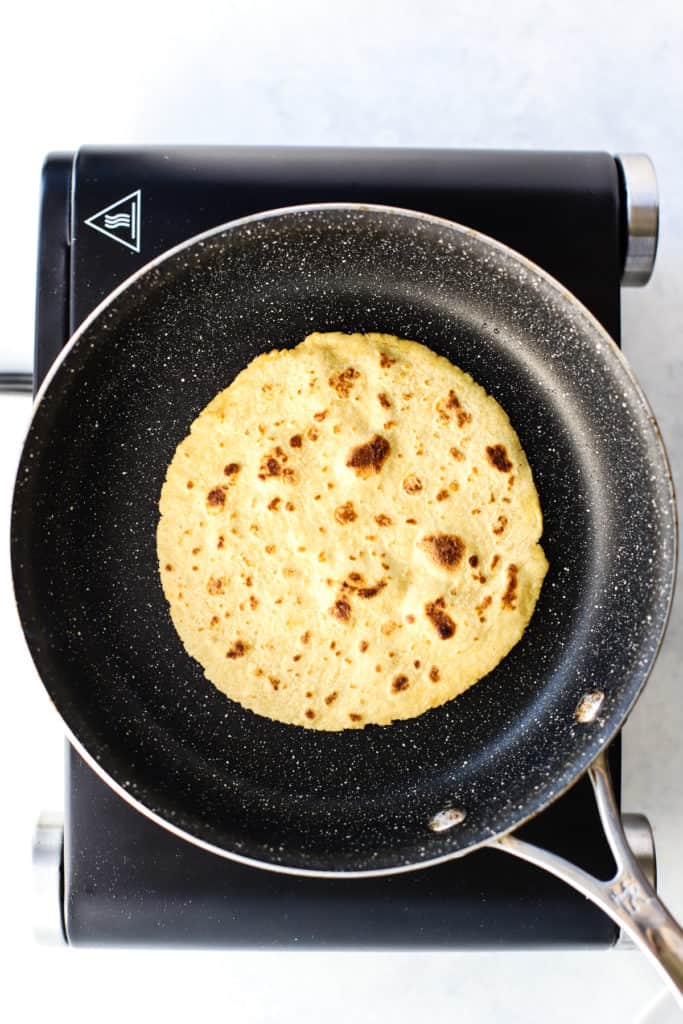 Corn tortilla frying in olive oil in black pan