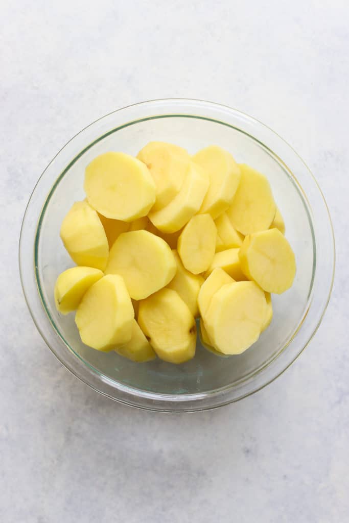 Sliced and peeled Yukon gold potatoes in clear glass bowl