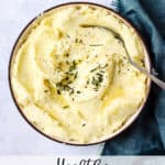 Healthy Instant Pot mashed potatoes in beige bowl with butter melted on top, chives, and pepper, with spoon & teal linen on side.