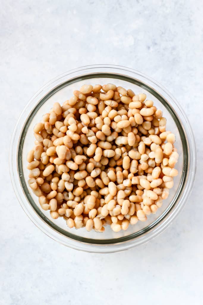 Navy beans, drained and rinsed, in clear glass bowl on light blue and white surface