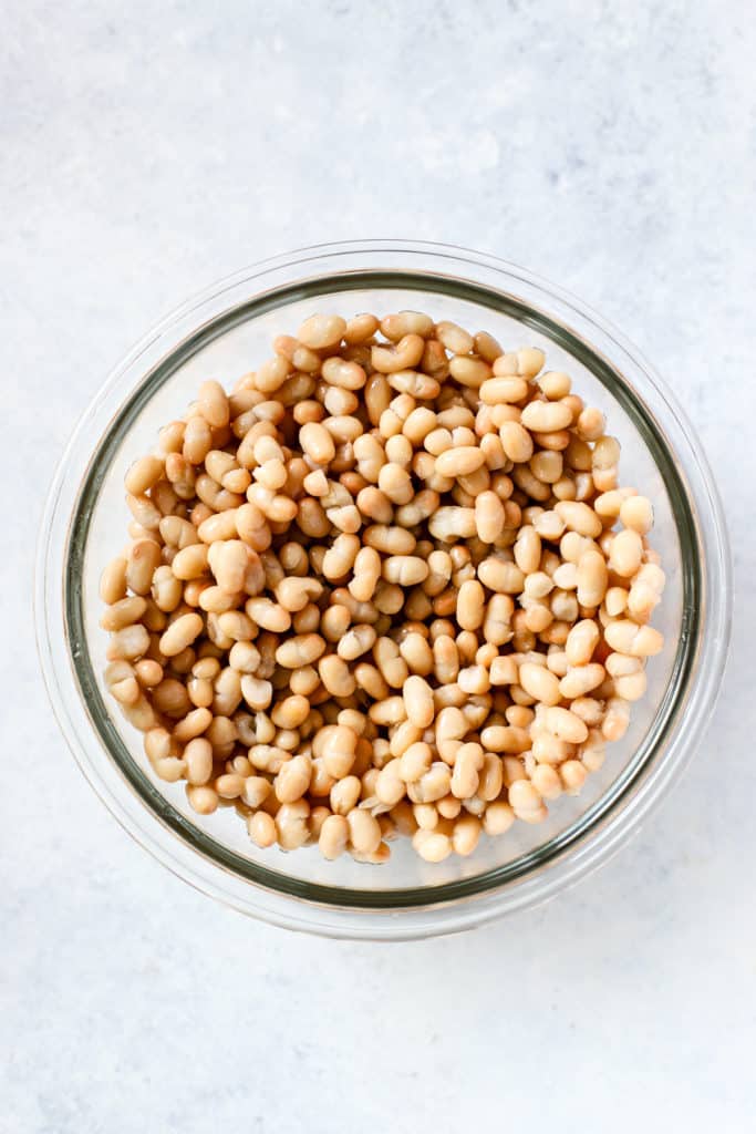 Navy beans, drained and rinsed, in clear glass bowl on light blue and white surface.