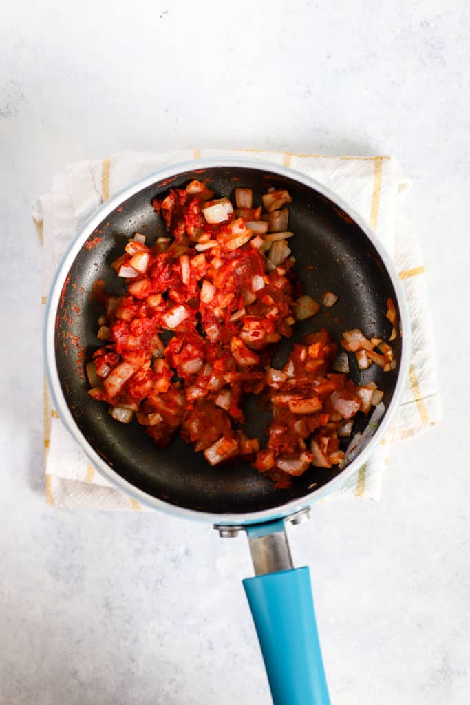 Sautéed onions and garlic in tomato paste in small pot with blue handle.