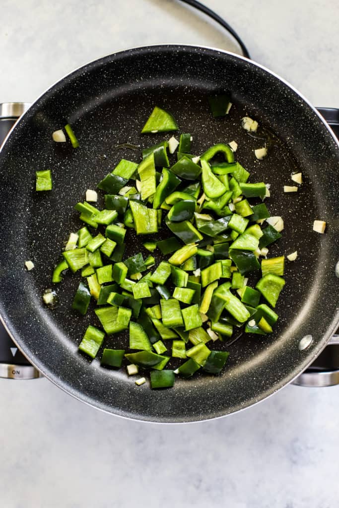 Poblano peppers and garlic being sautéed in black pan