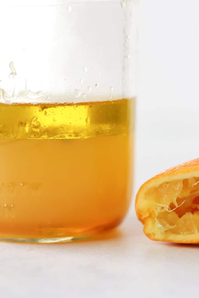 Simple orange vinaigrette in glass mason jar, not yet shaken, with juiced orange wedge on the side