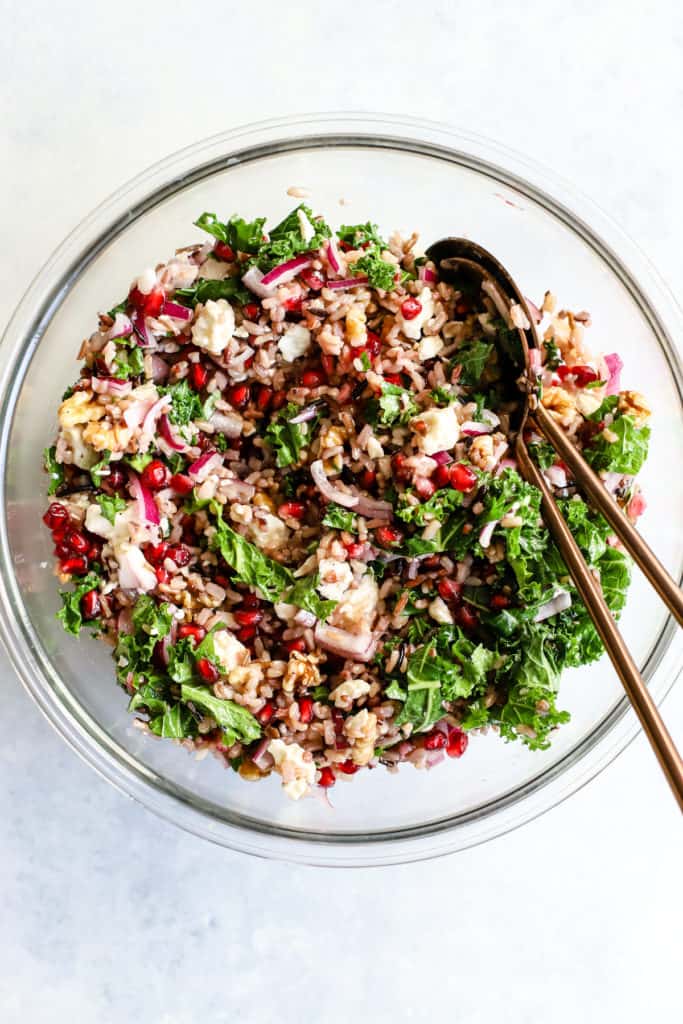 Wild rice and pomegranate salad in clear glass bowl with copper serving spoons