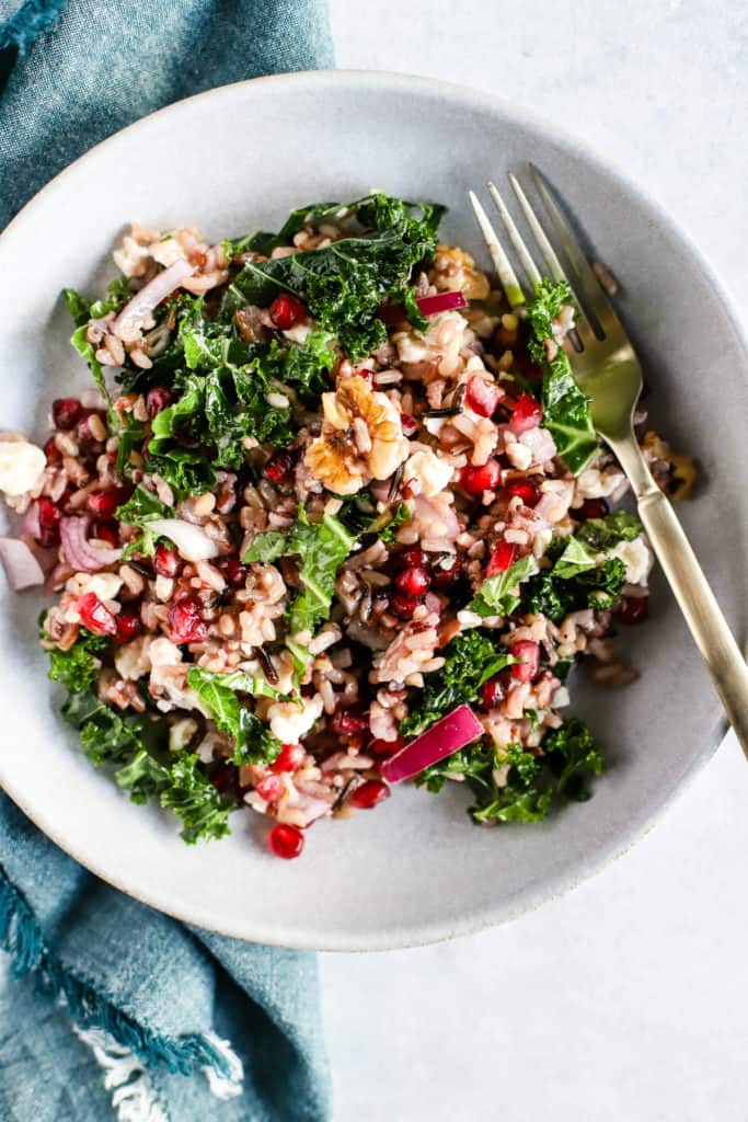 Wild rice and pomegranate salad in light blue bowl with gold fork and teal linen on the side