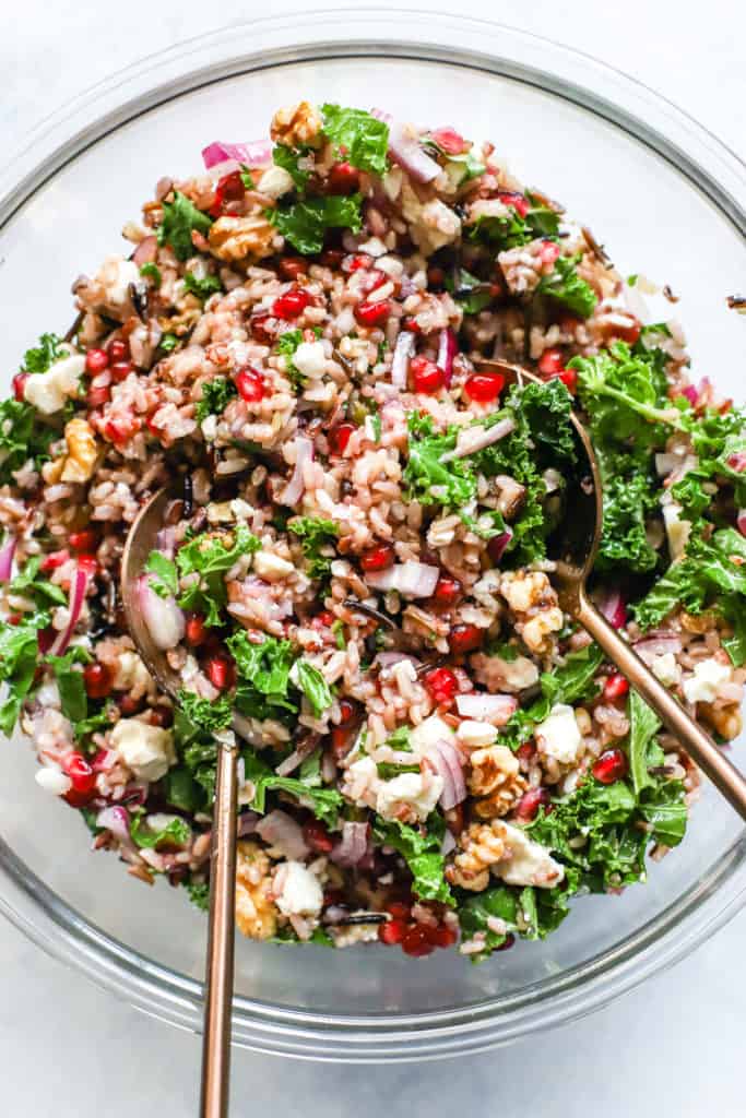 Wild rice and pomegranate salad in clear glass bowl with copper serving spoons