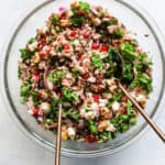 Wild rice and pomegranate salad in clear glass bowl with copper serving spoons