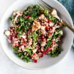 Wild rice and pomegranate salad in light blue bowl with gold fork and teal linen on the side