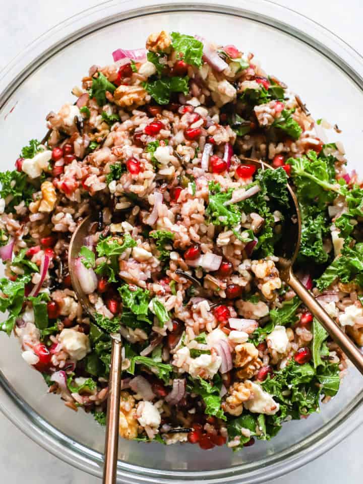 Wild rice and pomegranate salad in clear glass bowl with copper serving spoons