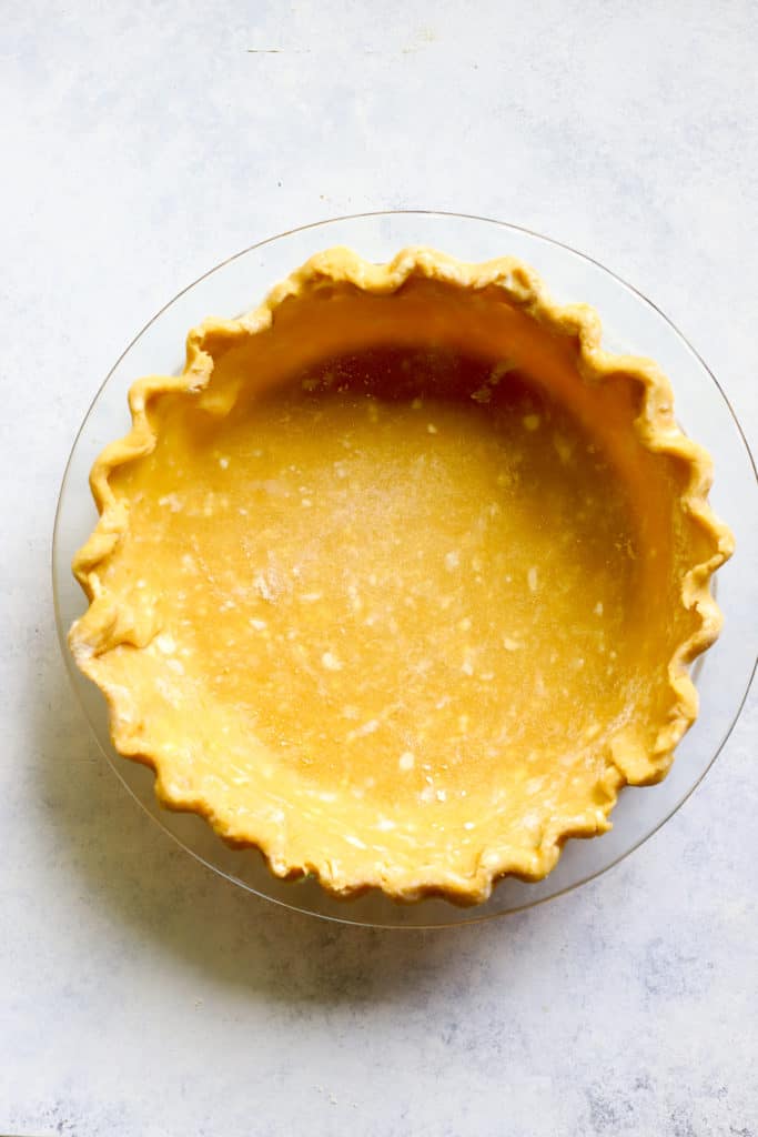 Chickpea flour pie crust in clear glass pie dish on blue and white surface