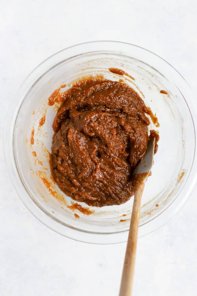 Almond butter cookies dough mixture in clear glass mixing bowl with spatula