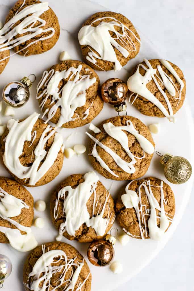 Flourless almond butter cookies, drizzled with white chocolate, on white marble surface with a few small ornaments and white chocolate chips sprinkled around