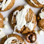 Flourless almond butter cookies drizzled with white chocolate, on white marble surface with small copper ornament and white chocolate chips sprinkled around