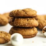 A stack of three healthier soft ginger molasses cookies, with more cookies in the background, on white marble surface with a few ornaments